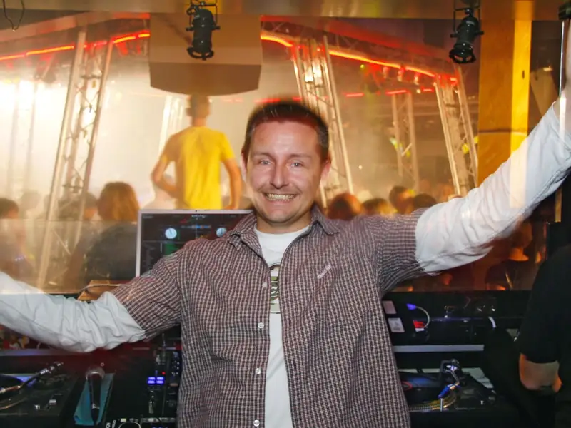 Markus Schumacher reißt hinter dem DJ-Pult einer großen Diskothek die Arme hoch