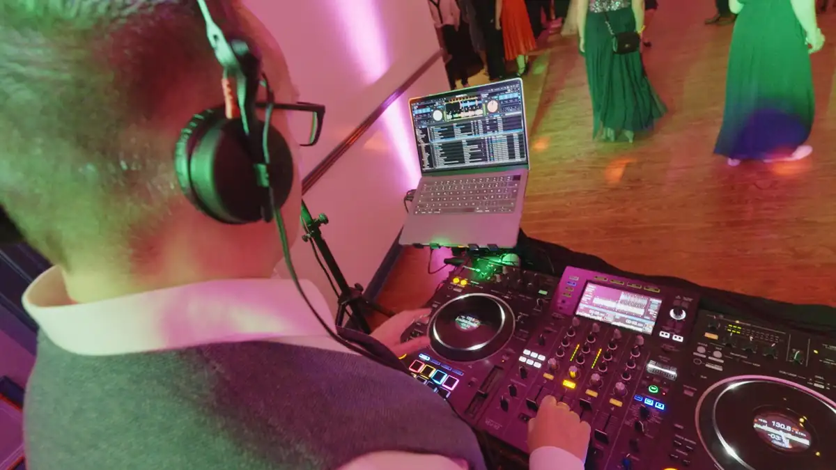 Markus Schumacher am DJ-Pult mit Kopfhörern und Laptop, im Hintergrund tanzen Gäste