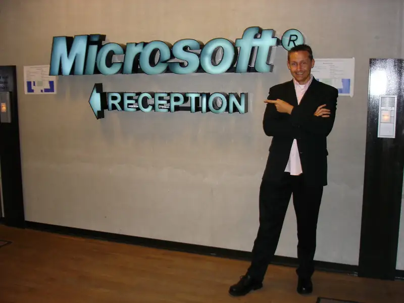 Markus Schumacher zeigt lächelnd auf das beleuchtete Microsoft-Schild an der Rezeption
