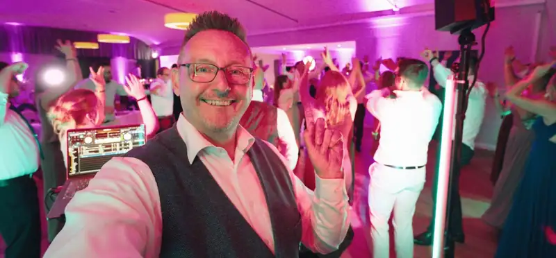 Markus Schumacher macht ein Selfie vor einer tanzenden Hochzeitsgesellschaft in pinkem Licht